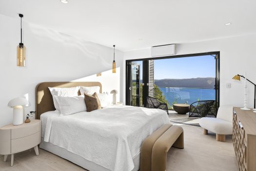 Modern bedroom with ocean view and balcony seating.